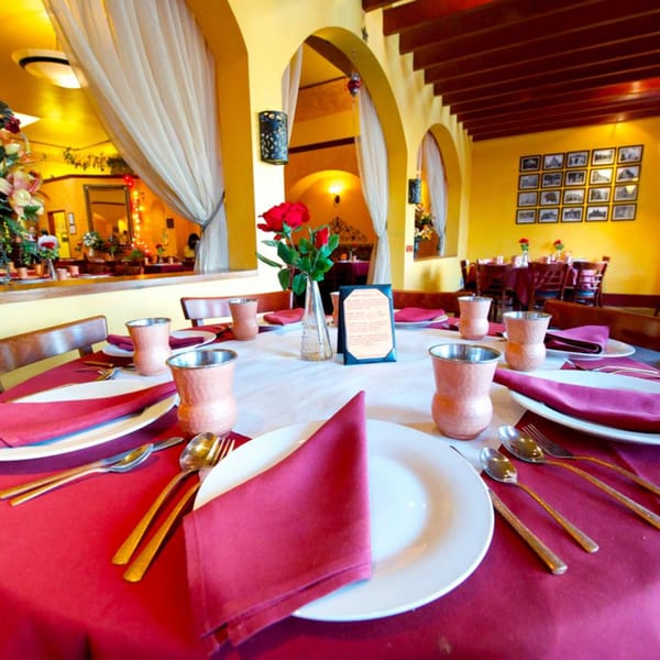 Set table with red tablecloth, white plates, copper cups, and a red rose centerpiece at Delhi Diner.