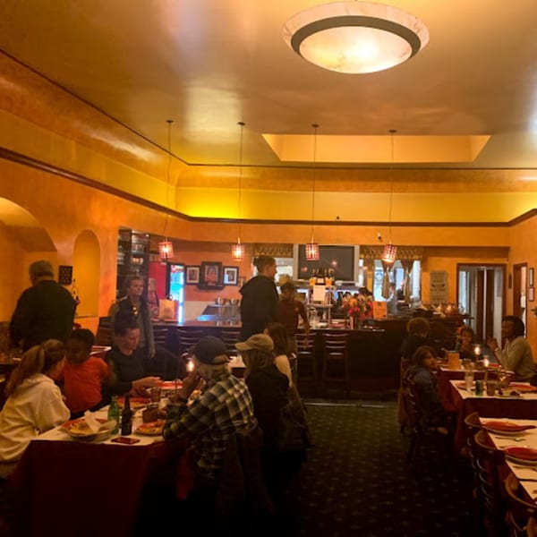 Warmly lit interior of Delhi Diner with patrons dining at tables and a bar area in the background.