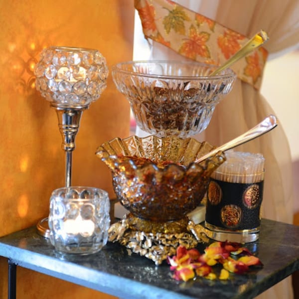 Decorative crystal bowls with Indian spices, candles, and rose petals on a dark table.