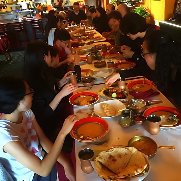 Diners enjoying Indian food at a long table in Delhi Diner, with various dishes and drinks.
