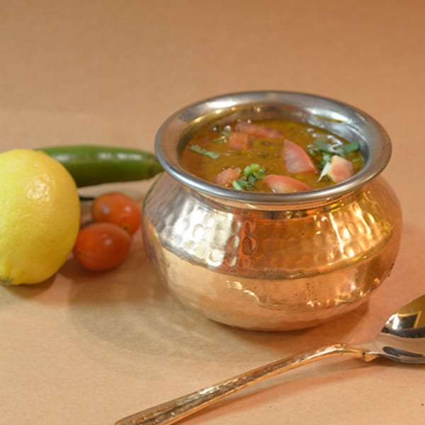 Indian lentil soup with tomatoes and cilantro in a hammered copper pot, with lemon and chili.