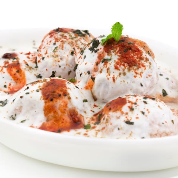 Dahi Vada, lentil fritters soaked in yogurt, topped with red chili powder and mint.