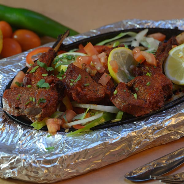 Delhi Diner's Indian lamb chops, garnished with lemon, tomatoes, and herbs, served on a sizzling platter.