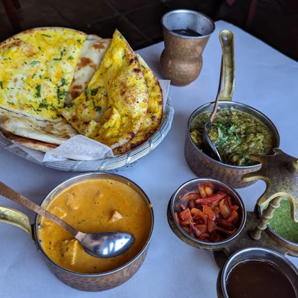 Indian dishes including naan bread, green and orange curries, and chutneys on a white table.