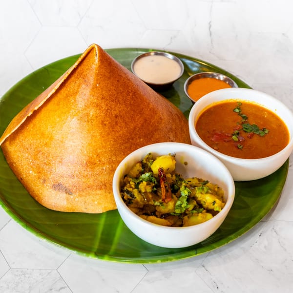 A golden-brown dosa, potato curry, sambar, and two chutneys on a green banana leaf plate.