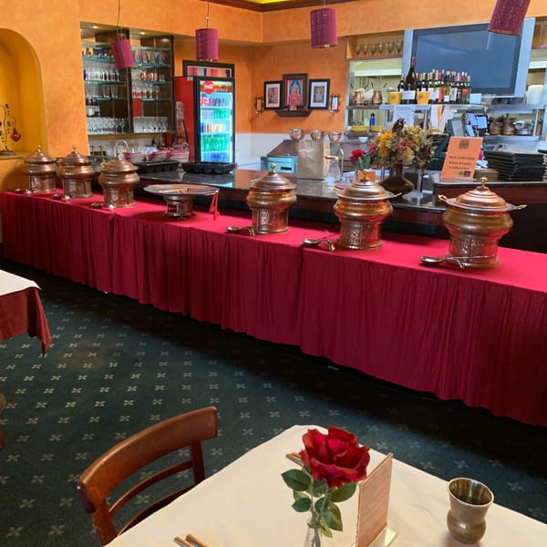A buffet line with copper chafing dishes on a red tablecloth, inside Delhi Diner restaurant.