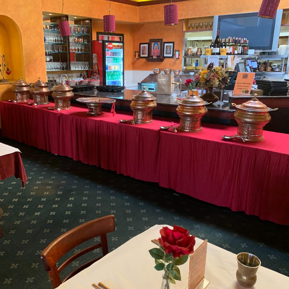 A buffet line with copper chafing dishes on a red tablecloth, inside Delhi Diner restaurant.