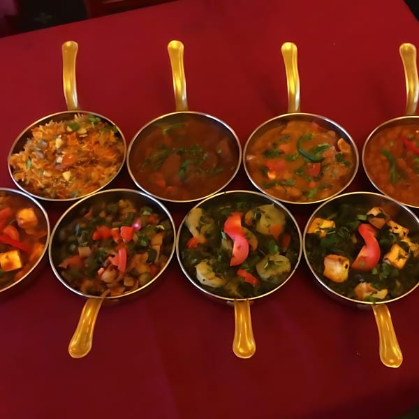 Seven Indian dishes in small golden-handled bowls, including curries, rice, and vegetables, on a red tablecloth.
